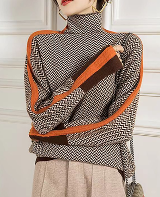 Blouse à col montant manches longues, motif chevrons noir et blanc, bordures orange et marron.
