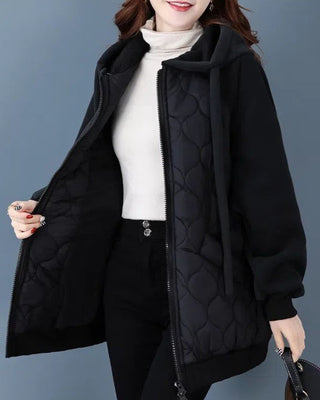 Veste matelassée à capuche noire, fermeture zippée, silhouette ample, coutures visibles.