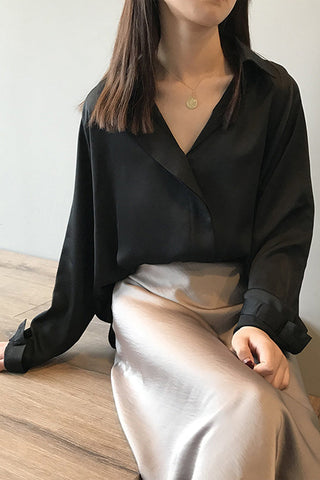 Blouse en satin noire manches longues, gros plan sur l’encolure en V boutonnée.