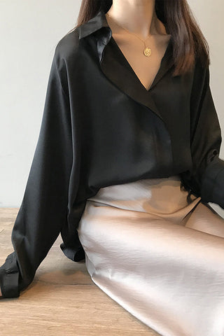Blouse en satin noir à manches longues, encolure en V boutonnée, allure fluide.