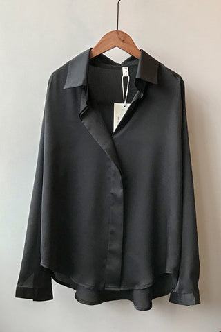 Blouse en satin noir manches longues sur cintre, col en V et fermeture boutonnée.