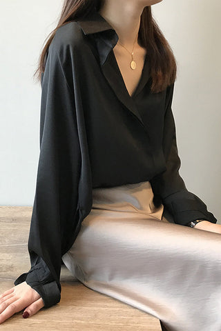Blouse en satin noir manches longues, col en V, porté avec jupe blanche assortie.