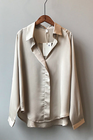 Blouse en satin champagne manches longues sur cintre, col en V, boutons visibles.