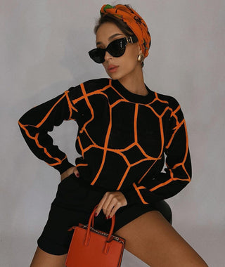 Blouse en maille noire à motifs géométriques orange, col rond côtelé, manches longues.