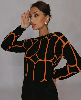 Blouse en maille noire à motifs géométriques orange, col rond, manches longues ajustées.
