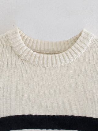 Encolure côtelée d’un pull en maille blanche avec bande noire rayée en bas de buste.