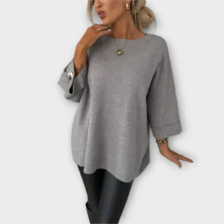 Blouse en maille grise à encolure ronde, manches 3/4 boutonnées, silhouette ample.