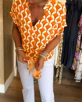 Chemisier à manches courtes, encolure V, motif géométrique orange et blanc sur tissu fluide.