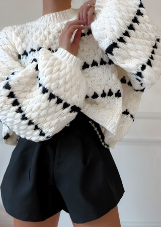 Pull en tricot vanille à motifs rayés noirs, manches ballon et encolure ras du cou.
