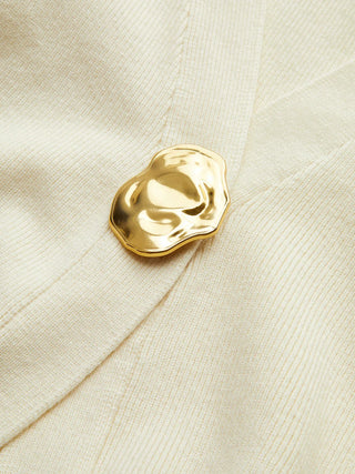 Bouton doré sur tissu beige, forme ovale texturée
