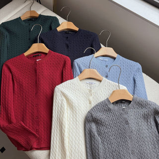 Gilets en tricot à torsades sur cintres, couleurs crème, rouge, bleu clair, gris et vert.