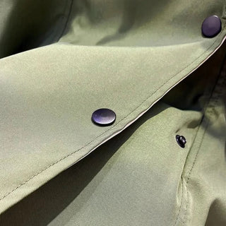 Détail patte avec boutons pression violets sur veste vert olive.
