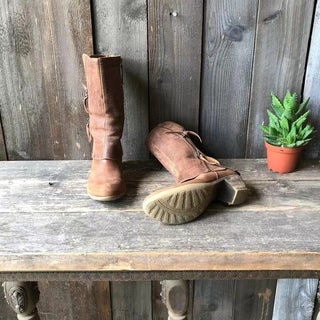Bottes marron hautes avec fermeture éclair latérale; semelle et talon visibles.