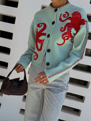 Cardigan bleu clair à boutons, motif pieuvre rouge sur le buste, ourlet contrasté.