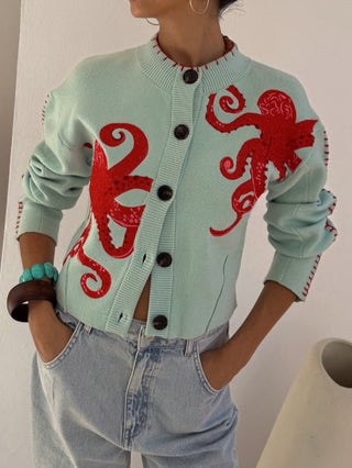 Cardigan en tricot bleu clair à boutons, motif pieuvres rouges sur la poitrine.