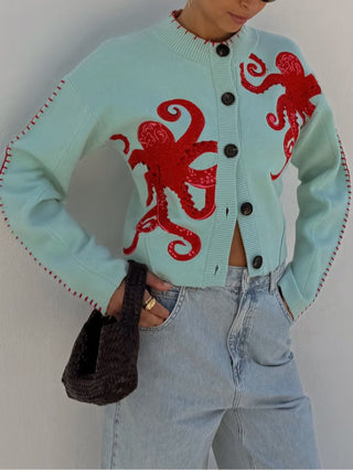 Cardigan bleu clair à boutons, grandes pieuvres rouges sur le devant, encolure côtelée.