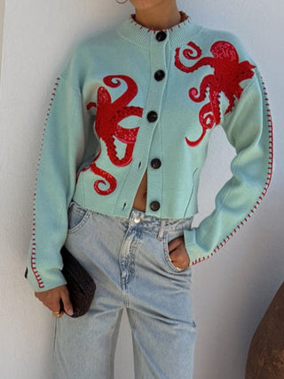 Cardigan tricot bleu clair boutonné, motif pieuvres rouges, poignets et ourlet contrastés.