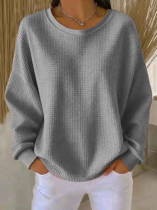 Pull en tricot gris à col rond, manches longues, texture maille et poignets côtelés.