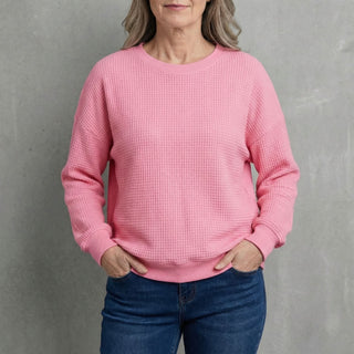 Pull en tricot rose à col rond, manches longues, poignets et ourlet côtelés.