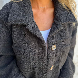 Manteau d’hiver gris foncé en tissu bouclé, col chemise, boutons et poches plaquées.