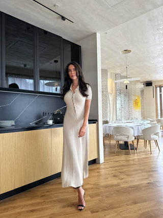 Robe longue beige en maille côtelée, col V boutonné, manches courtes, coupe près du corps.